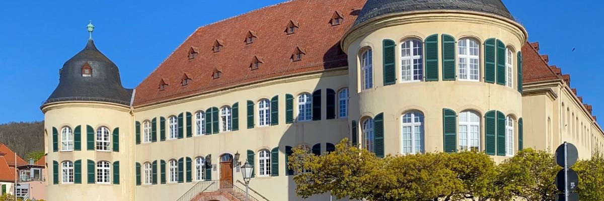 Ein altes Gebäude mit rechts und links jeweils einem breiten Turm. Im Hintergrund ist ein blauer Himmel zu sehen. 