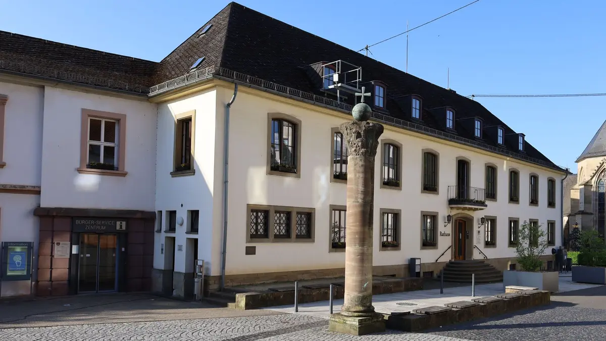 Historisches zweistöckiges Gebäude mit Schriftzug Rathaus. Links Anbau mit Schiebetüren. Davor Sandsteinsäule mit kupferner Kugel und Kreuz.   