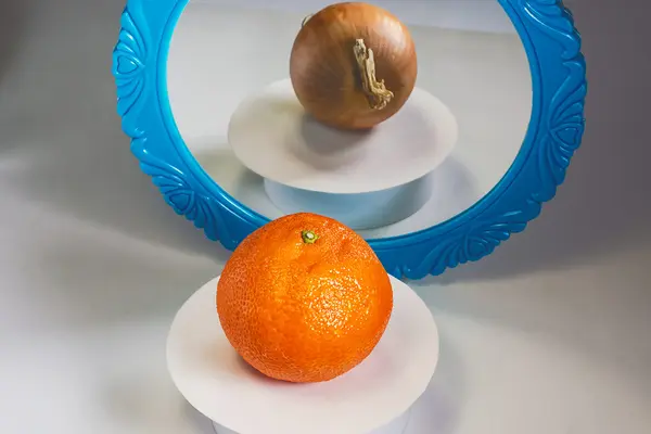 Täuschende Reflektion: vor dem Spiegel liegt Orange und im Spiegel sieht man eine Zwiebel