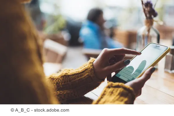 Eine Frau sitzt an einem Tisch und blickt auf ihr Smartphone.