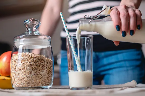 Frau gießt Milch oder Milchersatz aus einer Glasflasche in ein Glas