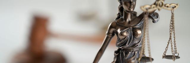Skulptur der Justizia, im Hintergrund ein Hammer als Symbol des Gerichtsurteils