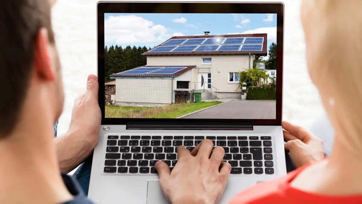 Ein Mann und eine Frau vor einem Laptop mit Foto eines Hauses mit Solardach