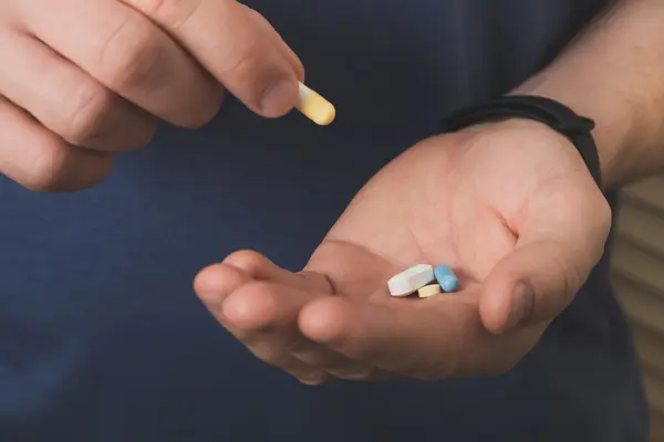Eine Männerhand legt eine Tablette mit Nahrungsergänzungsmittel in die andere Hand, in der weitere Tabletten liegen