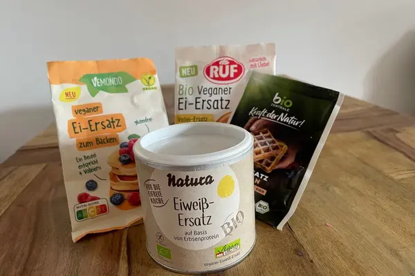Verschiedene Ei-Ersazprodukte in ihren Verpackungen auf einem Holztisch.