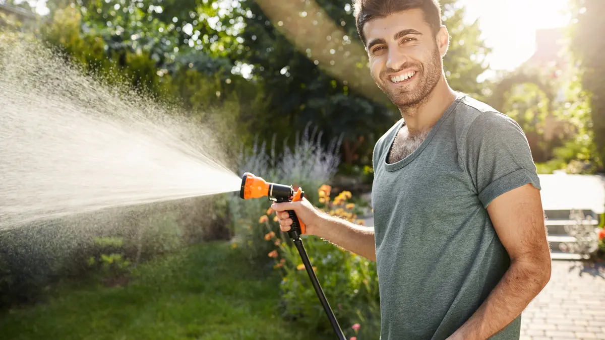 Mann mit Gartenschlauch lacht und gießt Garten