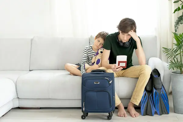 Zwei enttäuschte Jungs auf Sofa mit Koffer davor