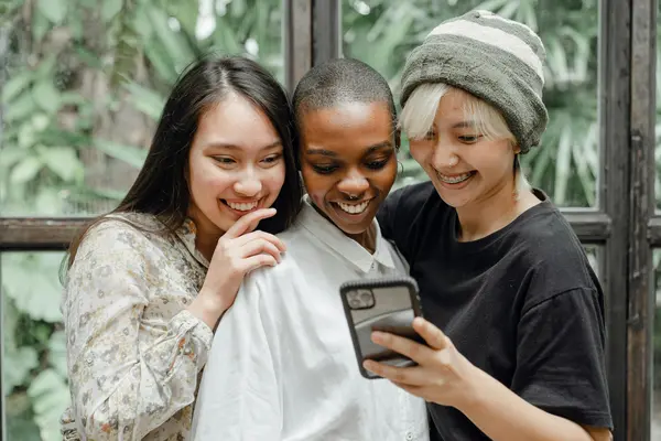 Drei Frauen, die lächelnd auf ein Smartphone schauen