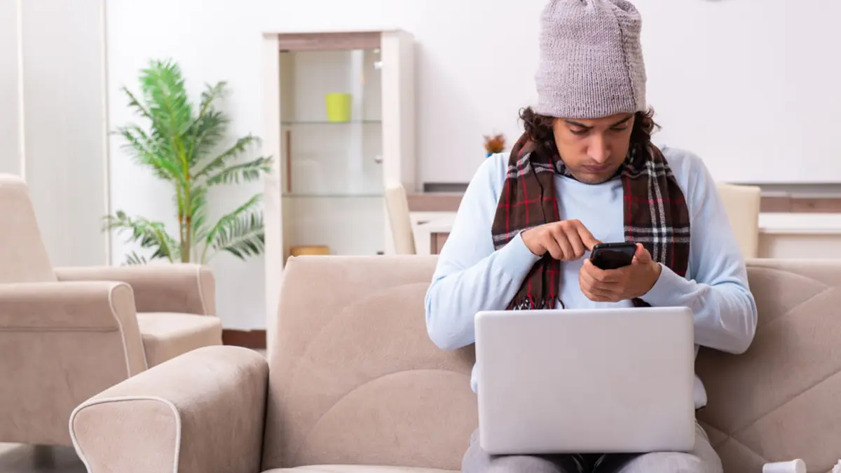 Mann mit Mütze und Schal am Laptop und Handy