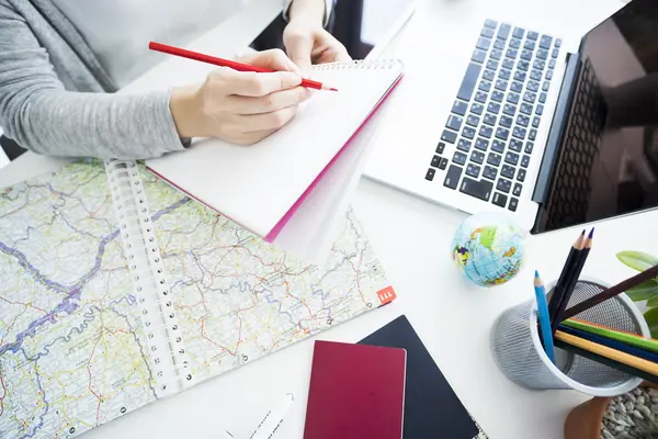 Frau bei der Reiseplanung_Bildausschnitt mit Karte, Laptop und Notizbuch