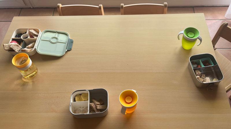 Auf einem Kindertisch stehen drei Brotboxen und Trinkgefäße