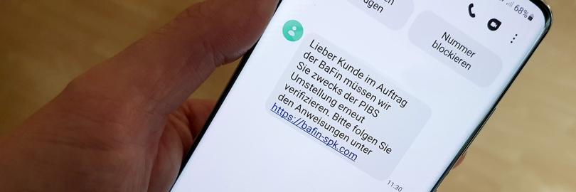 Hand hält Smartphone, Display zeigt betrügerische SMS zum Online-Banking