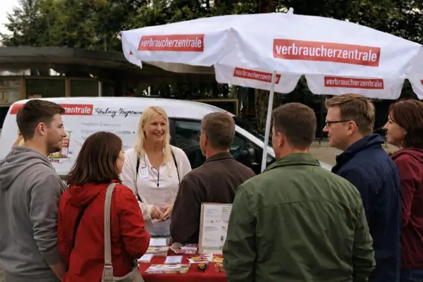Stand im Freien (Baüme im Hintergrund) mit einem Verbraucherzentralen Schirm
