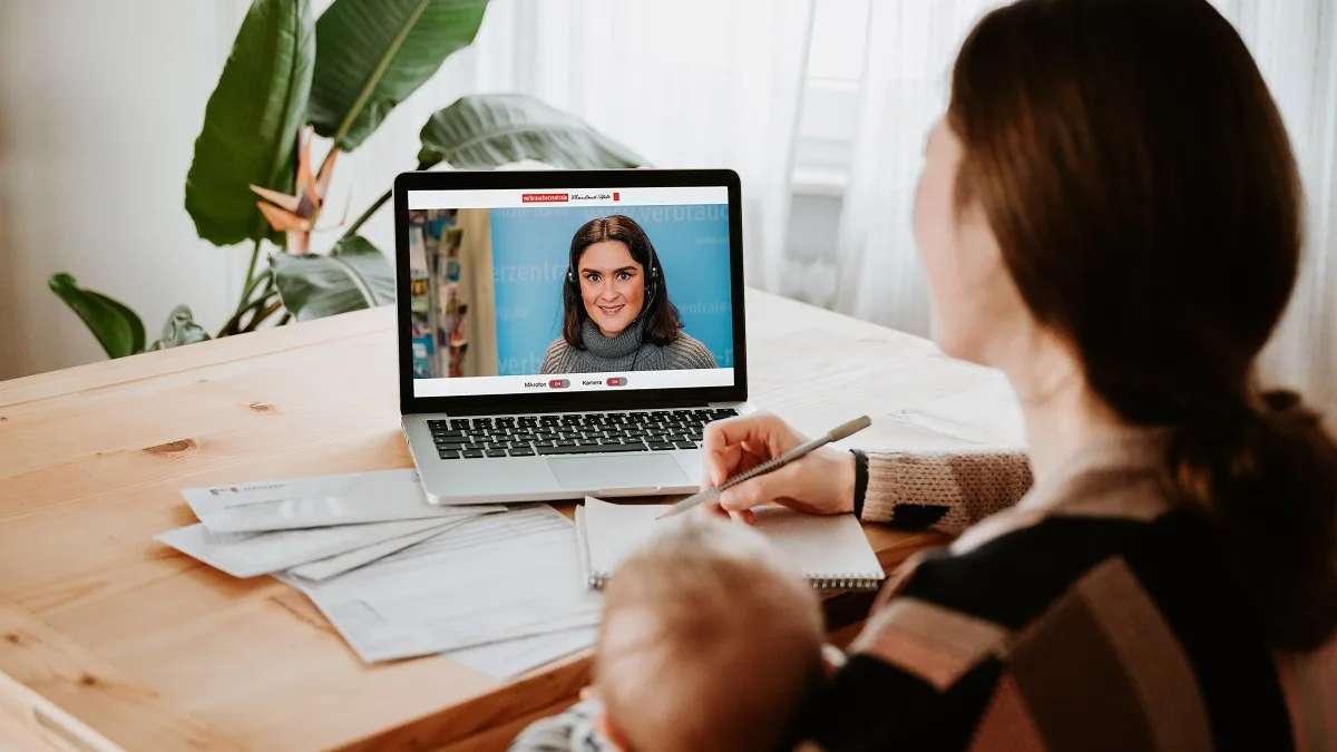 Frau sitzt mit Laptop an einem Tisch und unterhält sich per Video-Chat.