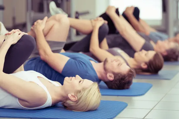Eine Gruppe Menschen liegt bei einem Sportkurs auf Trainingsmatten.