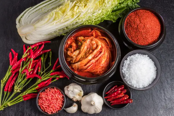 Auf einem Tisch liegen Kimchi, Chilis, Kohl und weitere Zutaten wie Knoblauch.