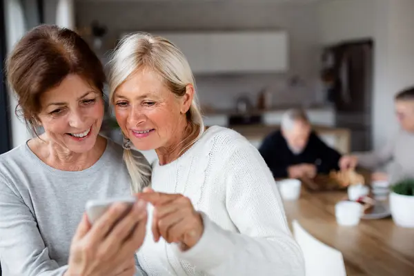 Zwei sportlich wirkende Frauen um die 70 schauen in der Küche gemeinsam auf ein Smartphone