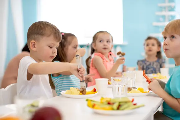 Kinder sitzen in der Kita am Tisch und essen