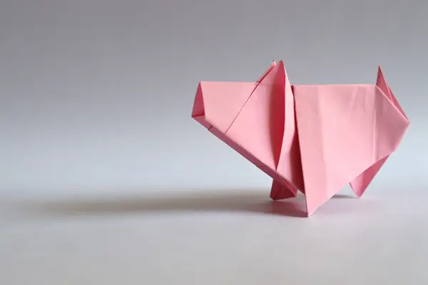 Ein rosa Schwein, gefaltet aus Papier von einem grauen Hintergrund