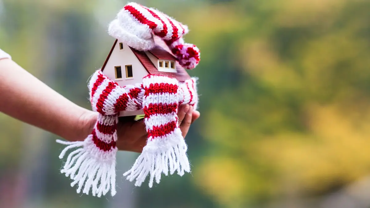 Ein kleines Haus mit einem Schal umwickelt auf einer Hand.