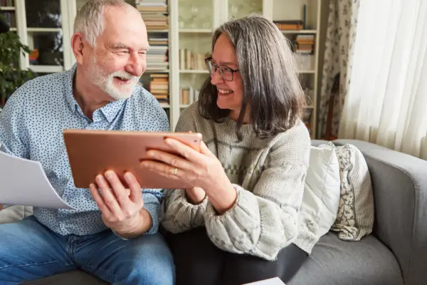 zwei ältere Menschen sitzen auf dem Sofa und haben ein Tablet in der Hand
