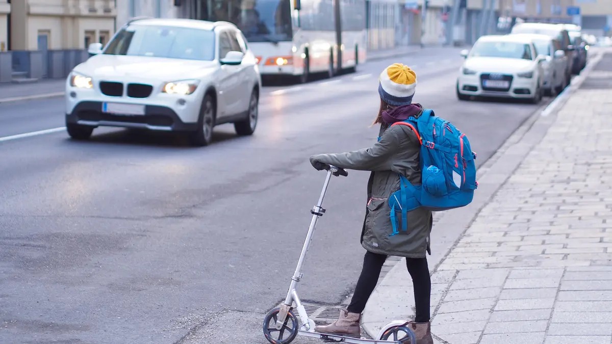 Kind überquert auf dem Schulweg mit einem Roller die Straße