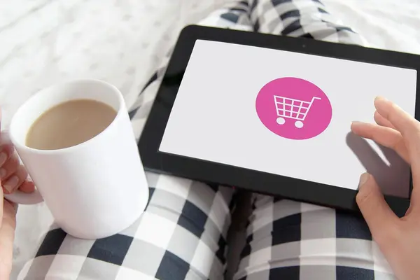 Tablet mit Einkaufswagen-Symbol auf Schoß mit karierter Schlafanzughose