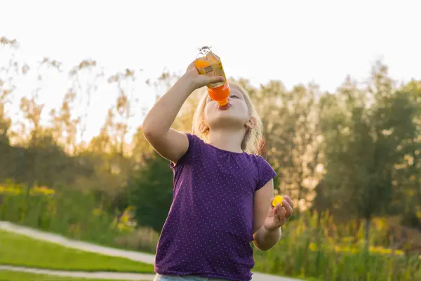 Kind trinkt draußen ein Kindergetränk, ähnlich Multivitaminsaft aus einer Flasche