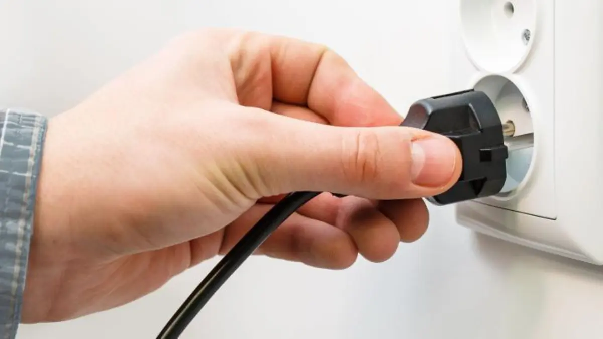 Hand hält Stecker an eine Steckdose