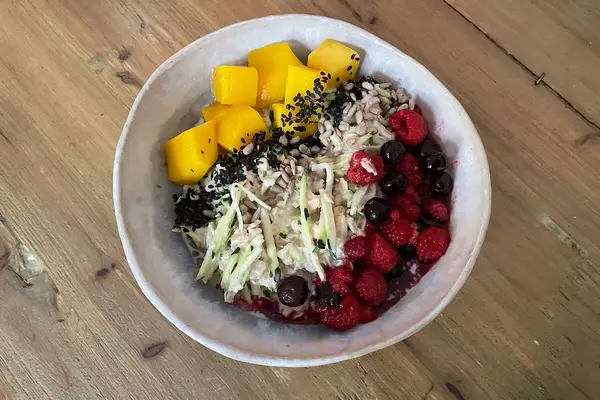 Ein Schüssel mit Haferbrei steht auf einem Tisch. Garniert ist der Brei mit Mango, Beeren und Zucchini.