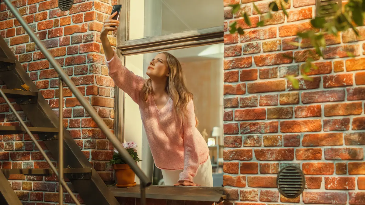 Frau lehnt sich aus dem Fenster und hält Handy nach oben.