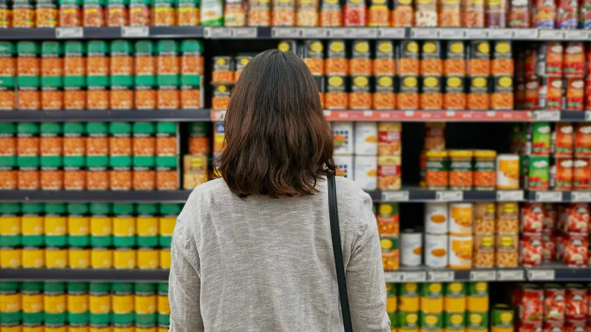 Eine Frau steht vor einem sehr großen Supermarktregal voller Fertigprodukte