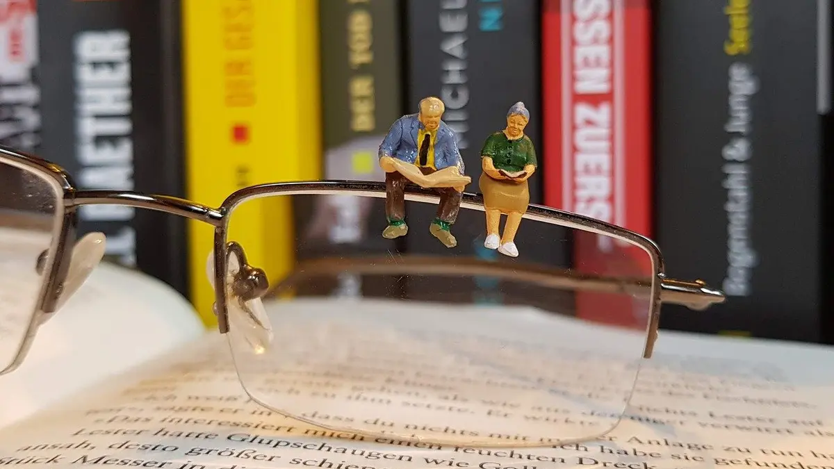 Figuren eines altes Ehepaars sitzt auf einer Brille, die auf Büchern liegt