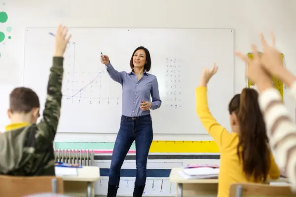 Lehrerin steht vor einer Klasse. Die Schulkinder zeigen auf.