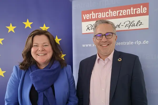 Eine Frau und ein Mann stehen vor einem Roll-up der Verbraucherzentrale und lächeln in die Kamera.