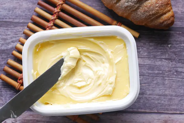 Eine offene Margarinepackung steht auf einem Tisch, ein Messer mit etwas Margarine liegt darauf.