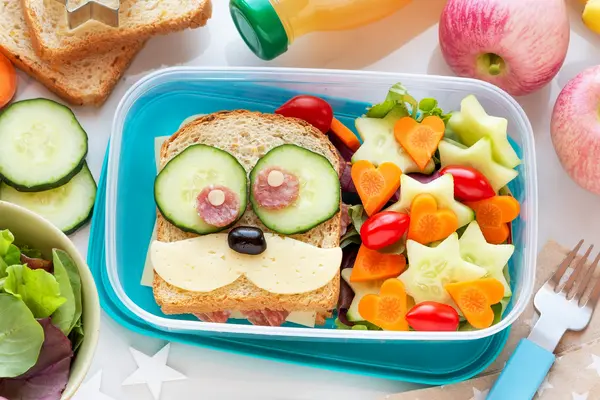 Eine geöffnete Brotbüchse mit einem Brot mit Augen aus Gurkenscheiben.