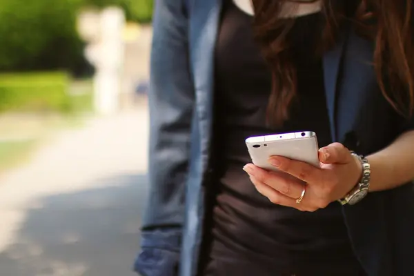 Frau geht mit einem Smartphone in ihrer Hand durch einen Park