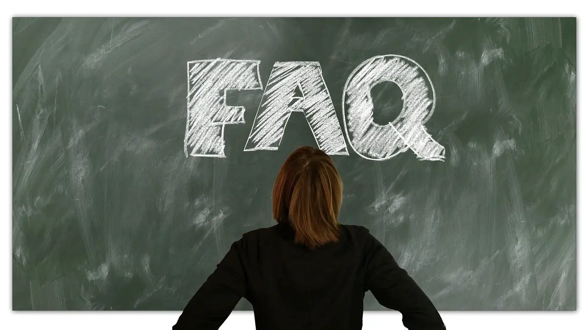 Eine Frau steht vor einer Tafel, auf der mit Kreide "FAQ" geschrieben wurde.