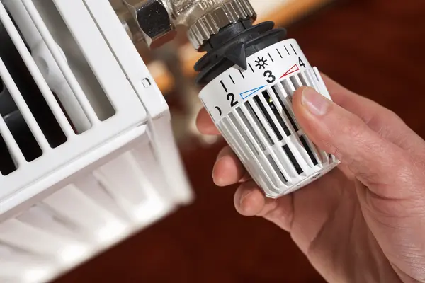 Eine Hand dreht am Thermostat einer Heizung