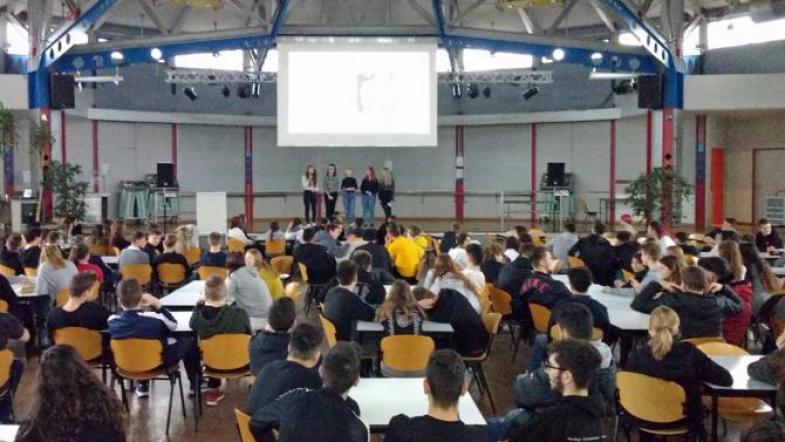 Schüler/-innen stehen auf einer Bühne vor ihren Mitschüler/-innen