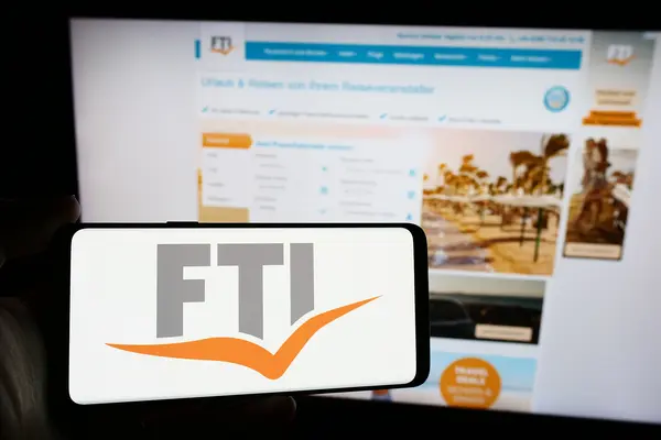 Das Foto zeigt im Vordergrund das Logo der FTI Touristik auf einen Smartphone, im Hintergrund ist die Homepage der FTI Touristik zu sehen