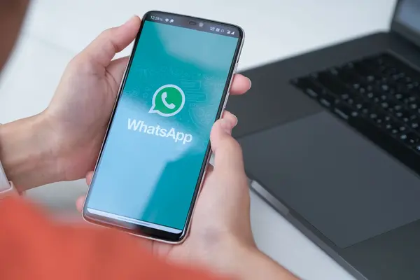 Jemand hält ein Handy in der Hand, auf dessen Display das WhatsApp-Logo zu sehen ist