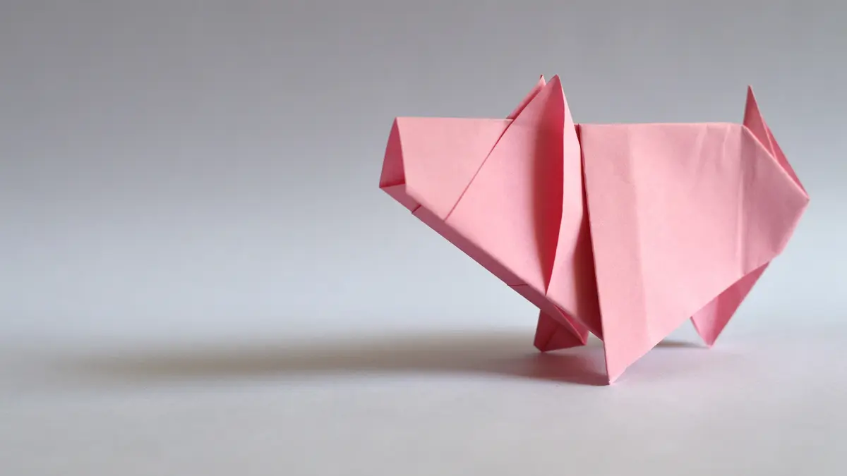 Ein rosa Schwein, gefaltet aus Papier von einem grauen Hintergrund