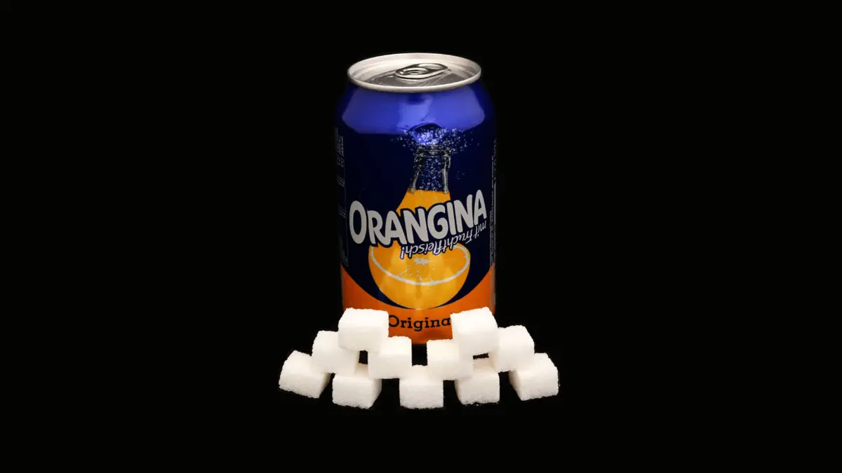 Dose Orangina auf schwarzem Grund mit 11 Zuckerwürfeln davor