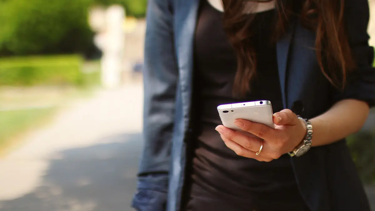 Frau geht mit einem Smartphone in ihrer Hand durch einen Park