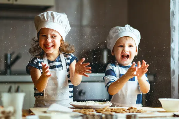 Zwei Kinder werfen Mehl in der Küche durch die Luft und backen