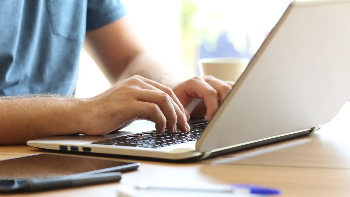 Mann schreibt auf Laptop, nur Hände sind sichtbar