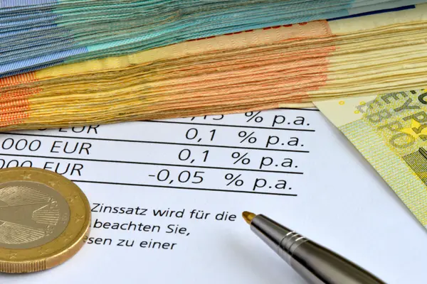 Münzen und ein Kugelschreiber liegen auf Blatt mit Zins-Informationen einer Bank