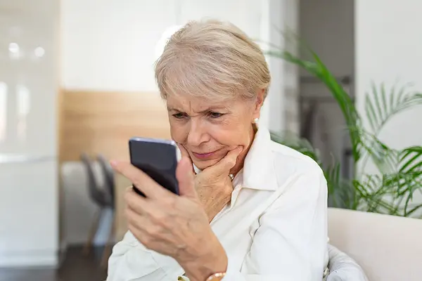Eine ältere Frau schaut kritisch auf ihr Smartphone